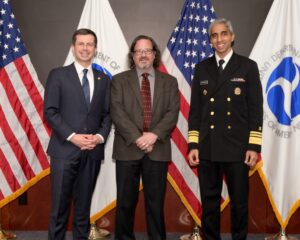 U.S. Secretary of Transportation Pete Buttigieg and Surgeon General Vice Admiral Vivek H. Murthy pose for a photo with ClassiCanadian blog author Brian Tetreault in front of United States and Department of Transportation flags in February of 2023